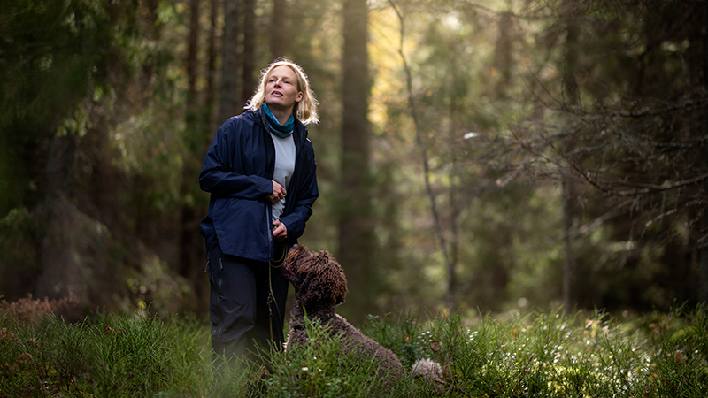 Kvinna i skogen med hund i koppel