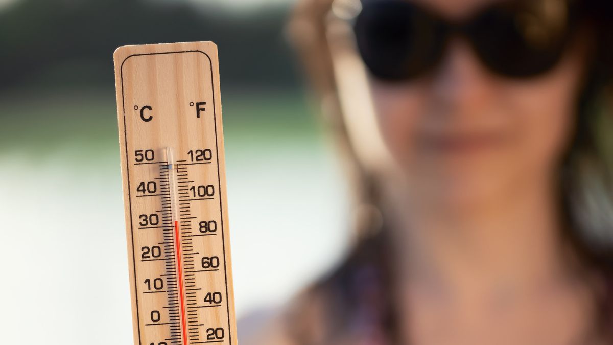 Termometer som visar hög temperatur med en person i solglasögon i bakgrunden.