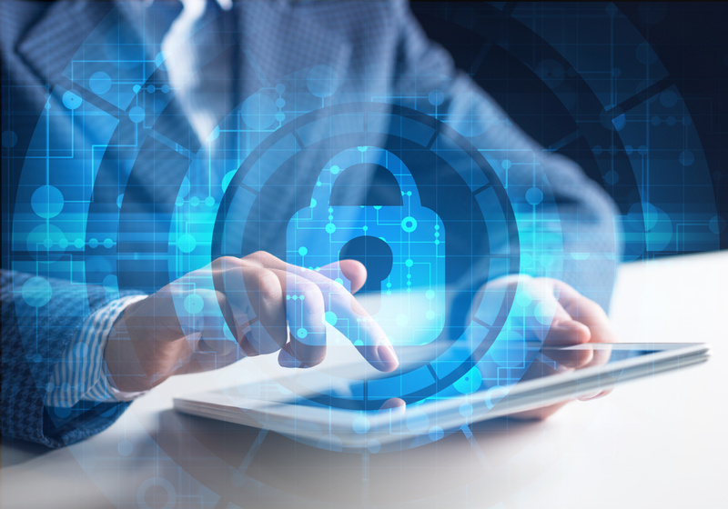 En person använder en surfplatta, med ett överlagt grafiskt motiv av ett hänglås och digitala nätverksmönster som symboliserar cybersäkerhet och skydd mot cyberangrepp.