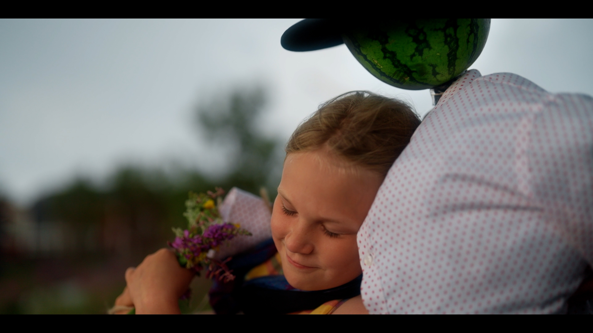 Flicka håller en bukett blommor och lutar huvudet mot en figur med melonhuvud