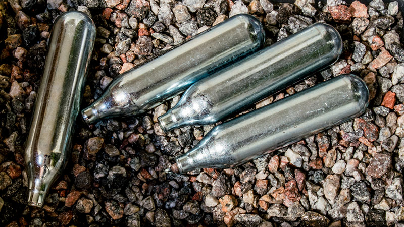 Silverfärgade lustgaspatroner ligger på marken