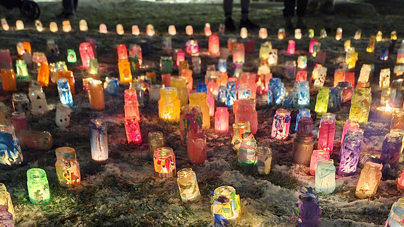 Färgglada ljuslyktor står på mark täckt av snö.