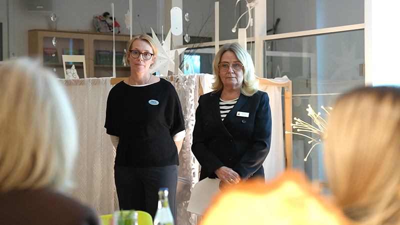 Två blonda kvinnor med namnbrickor talar inför publik.