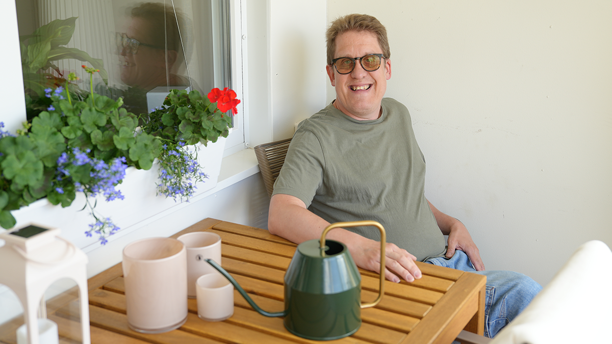 En man ler mot kameran från en stol på balkongen. 