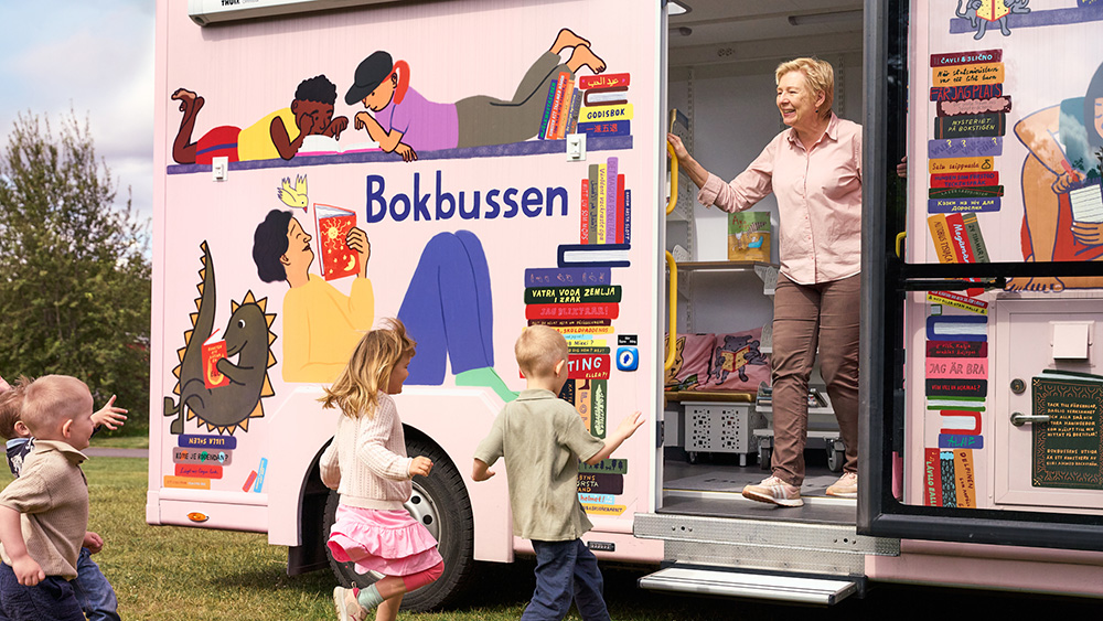 Barn som springer in i en färgglad buss där det står Bokbussen.
