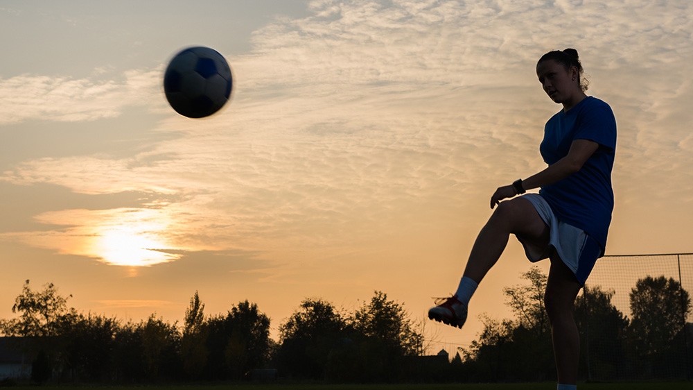 Tjej som spelar fotboll i motljus.